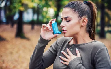 A woman using an asthma inhaler in the park.