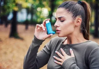 A woman using an asthma inhaler in the park.